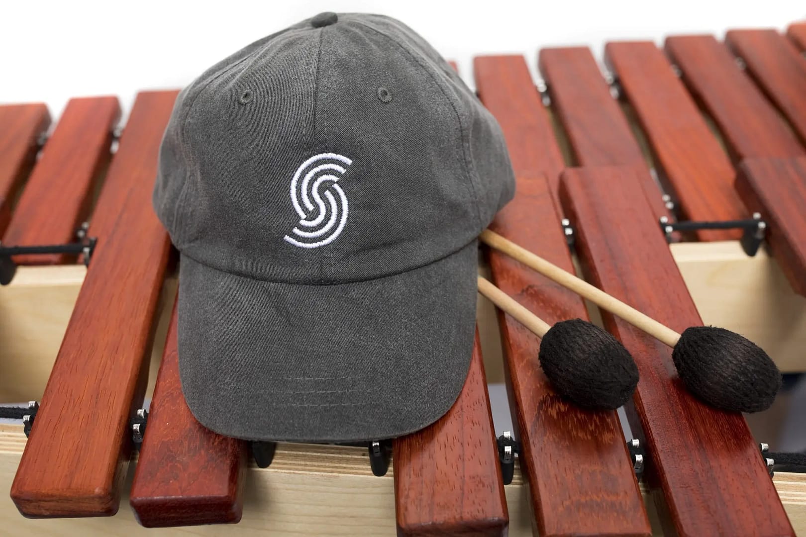 A baseball hat with a Sonaris logo and mallets sitting on top of a marimba